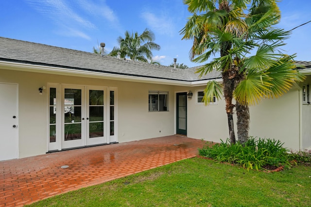 rear view of property featuring stucco siding, a lawn, a patio, french doors, and a shingled roof