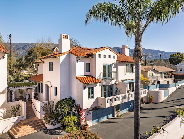 exterior space with an attached garage, a tiled roof, a chimney, a balcony, and a mountain view