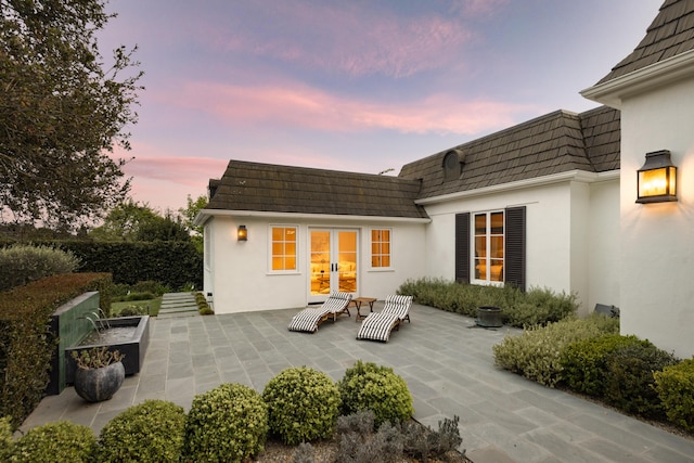 rear view of property featuring mansard roof, stucco siding, french doors, and a patio area