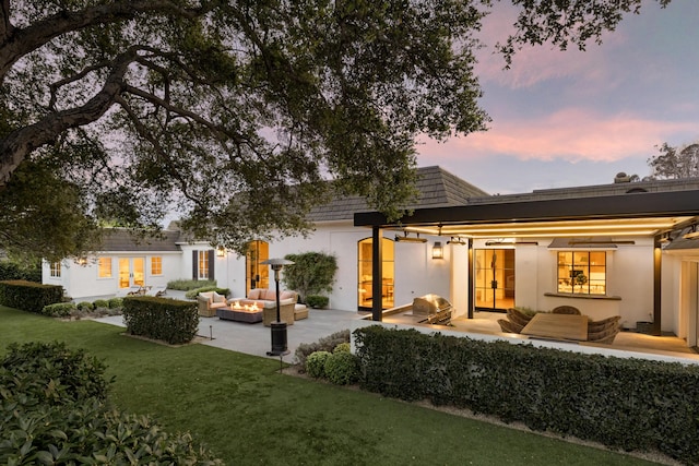 rear view of house featuring stucco siding, a lawn, french doors, outdoor lounge area, and a patio area