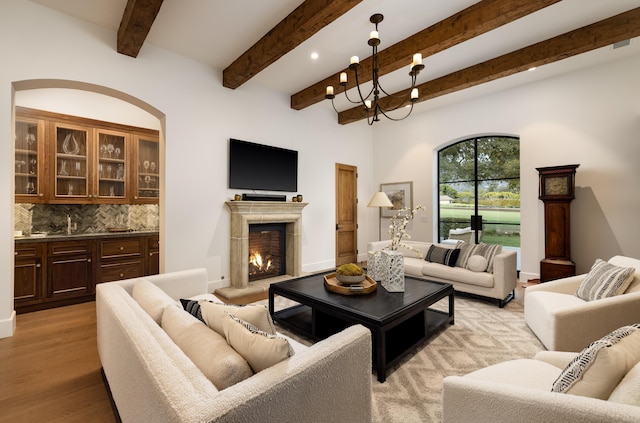 living room featuring recessed lighting, a lit fireplace, beamed ceiling, a notable chandelier, and light wood-type flooring