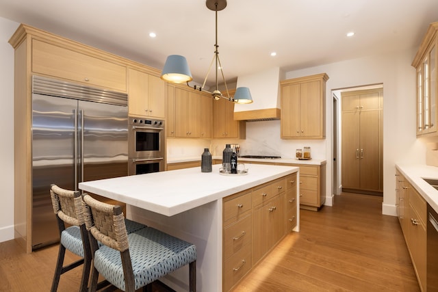 kitchen featuring light brown cabinets, custom exhaust hood, light wood-style flooring, appliances with stainless steel finishes, and a center island