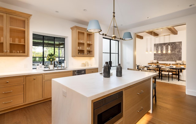 kitchen featuring stainless steel microwave, wood finished floors, light countertops, and a sink