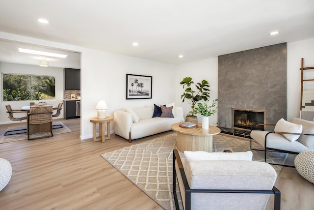 living room featuring recessed lighting, baseboards, a fireplace, and light wood finished floors