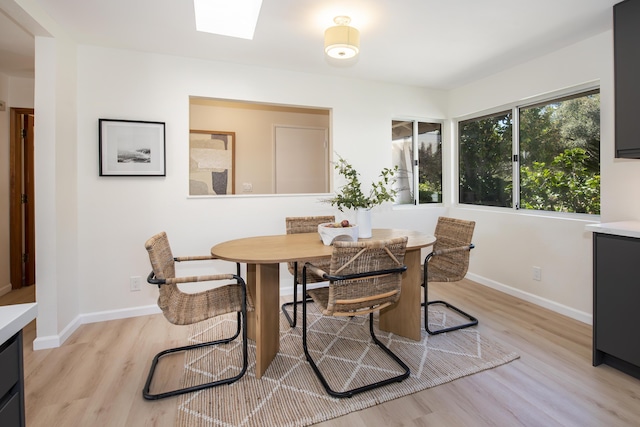 dining area featuring light wood-style flooring, a skylight, and baseboards