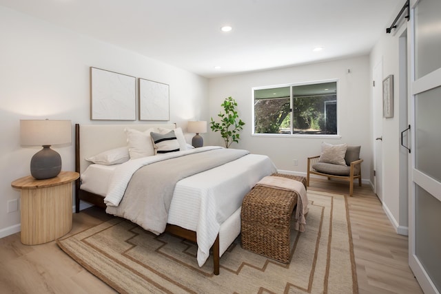 bedroom featuring light wood-type flooring, a barn door, baseboards, and recessed lighting