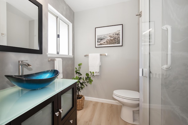 bathroom with a shower with door, baseboards, toilet, wood finished floors, and vanity