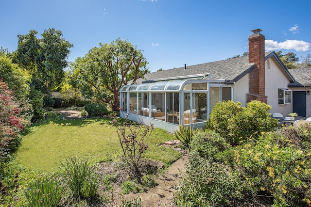 back of property featuring stucco siding, a sunroom, a yard, a shingled roof, and a chimney