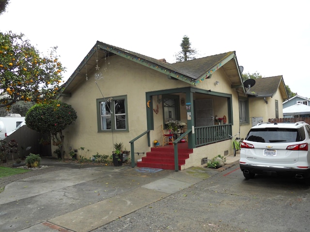 bungalow featuring stucco siding, a shingled roof, and fence