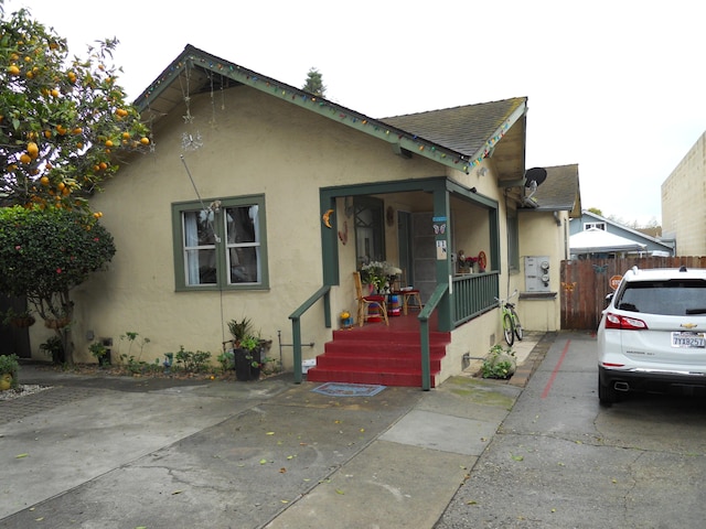 bungalow-style home with stucco siding, roof with shingles, and fence