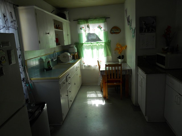 kitchen with white microwave, open shelves, freestanding refrigerator, decorative backsplash, and white cabinets