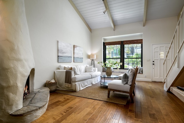 living area with high vaulted ceiling, a lit fireplace, stairs, hardwood / wood-style flooring, and beamed ceiling