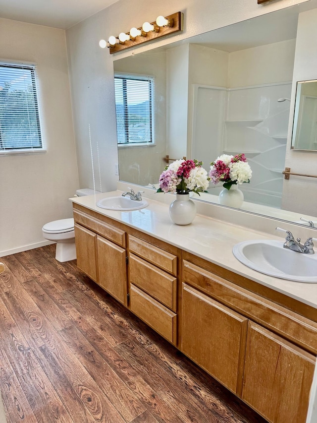 bathroom with double vanity, toilet, wood finished floors, and a sink