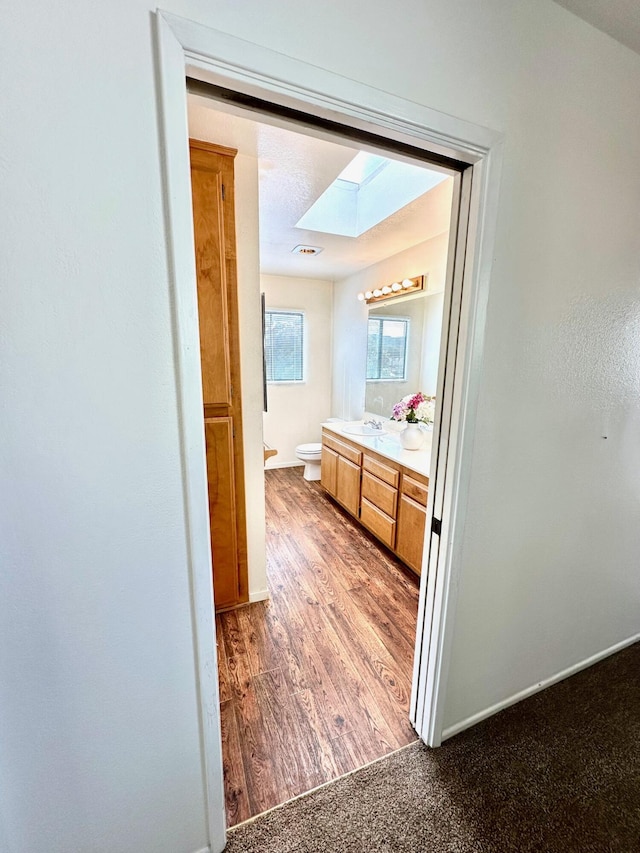 bathroom with visible vents, toilet, a skylight, wood finished floors, and vanity