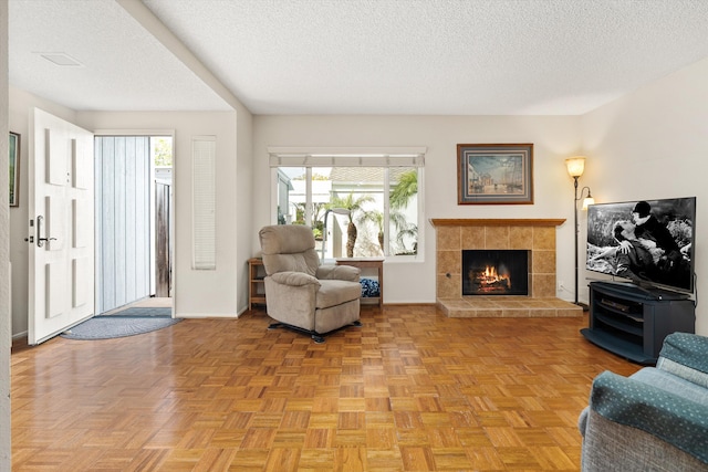 living area featuring baseboards, a textured ceiling, and a tiled fireplace