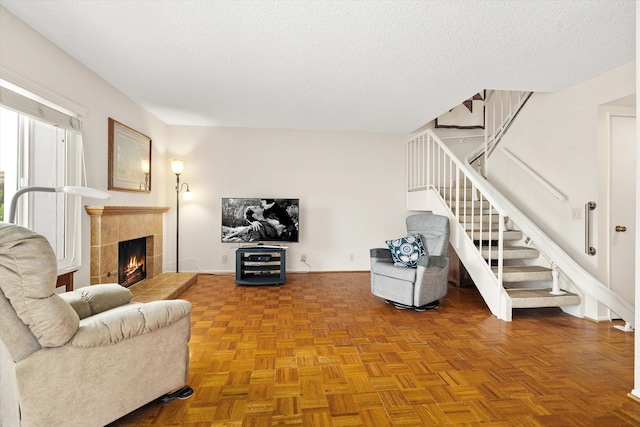 living area featuring a tiled fireplace, stairs, and a textured ceiling