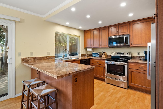 kitchen with brown cabinetry, a peninsula, ornamental molding, a sink, and appliances with stainless steel finishes