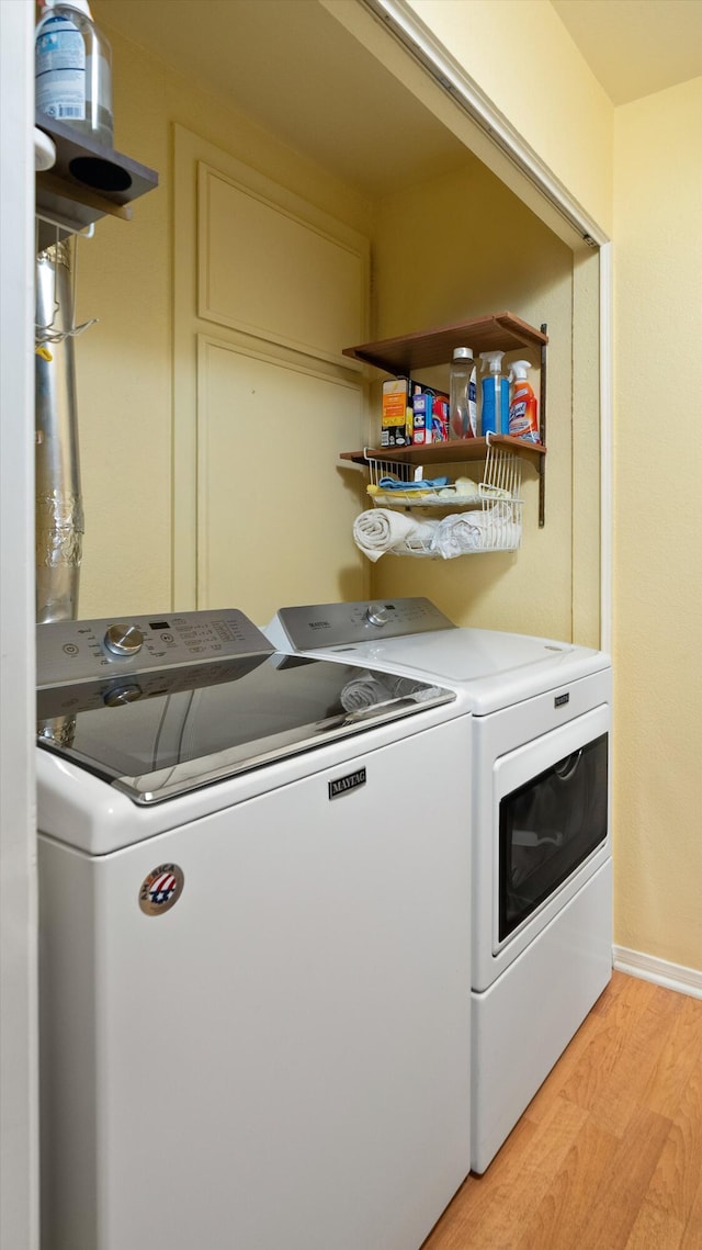 clothes washing area featuring light wood-style flooring, baseboards, and washer and clothes dryer