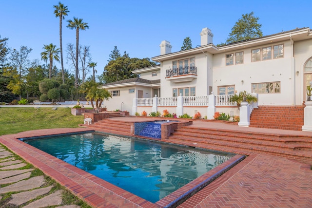 rear view of house featuring stucco siding, a chimney, a balcony, an outdoor pool, and a patio