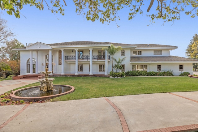 view of front facade with stucco siding, a balcony, and a front yard