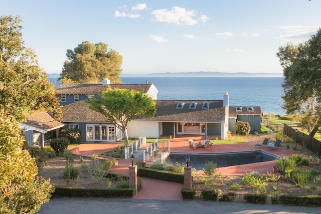 rear view of property featuring a fenced in pool, fence, french doors, a water view, and a patio area