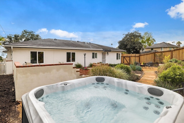 back of house with stucco siding, a hot tub, a deck, and fence