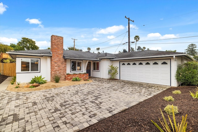 single story home with stucco siding, decorative driveway, an attached garage, a shingled roof, and a chimney