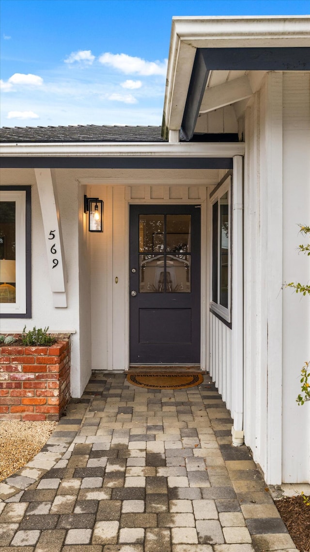 view of exterior entry with covered porch, board and batten siding, and roof with shingles