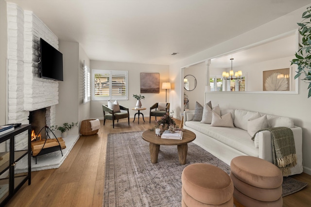 living area featuring a stone fireplace, plenty of natural light, an inviting chandelier, and hardwood / wood-style flooring