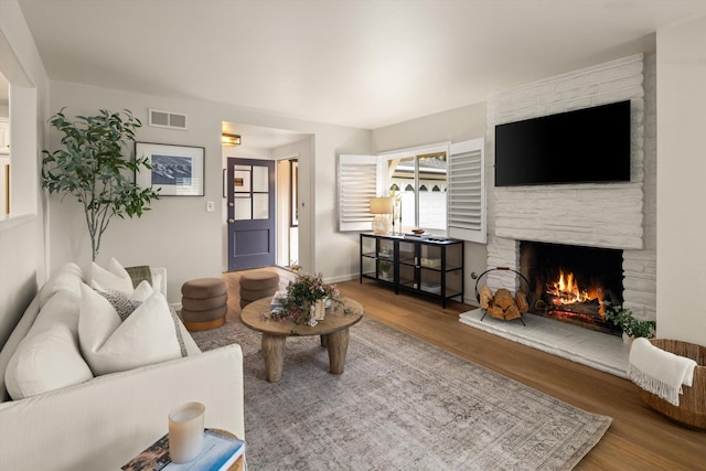 living area featuring a stone fireplace, wood finished floors, visible vents, and baseboards