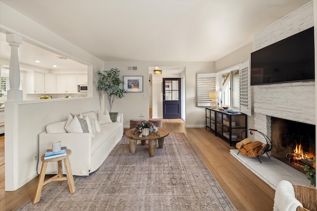 living room with wood finished floors, visible vents, baseboards, a fireplace, and recessed lighting