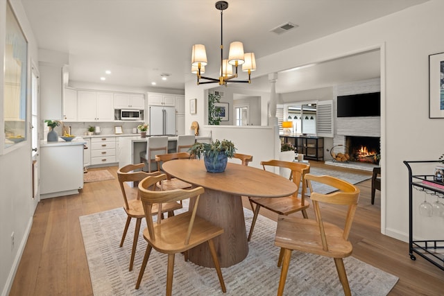 dining area featuring recessed lighting, visible vents, light wood-style floors, and a lit fireplace