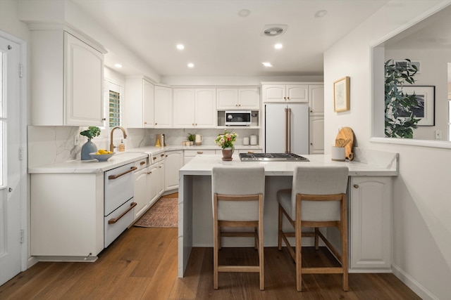 kitchen with backsplash, dark wood finished floors, a kitchen breakfast bar, white cabinets, and white appliances