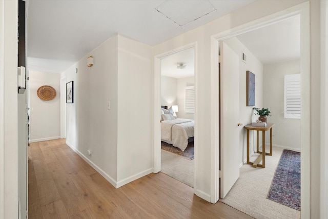 hall with visible vents, baseboards, and light wood-style floors