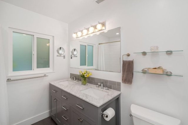 full bathroom featuring double vanity, toilet, baseboards, and a sink