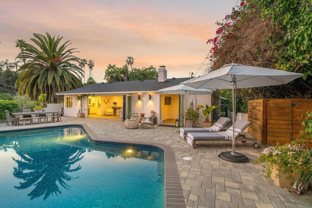 pool at dusk featuring an outdoor pool, fence, and a patio area