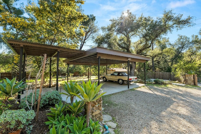 view of vehicle parking with a carport, gravel driveway, and fence