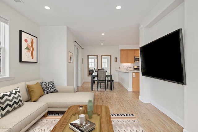 living room with recessed lighting, a barn door, baseboards, and light wood-style flooring