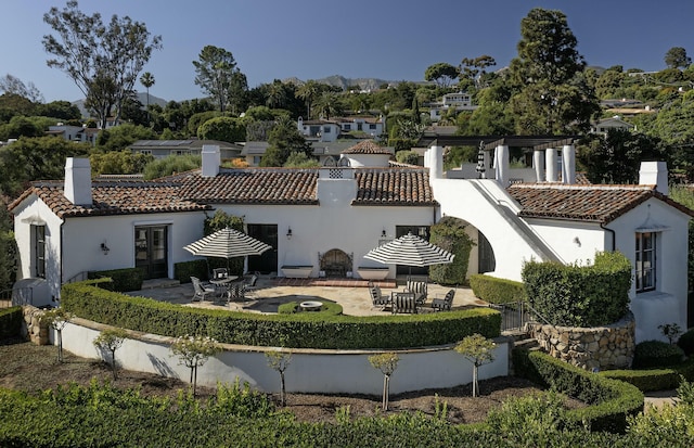 back of house with stucco siding, a tile roof, a chimney, and a patio area