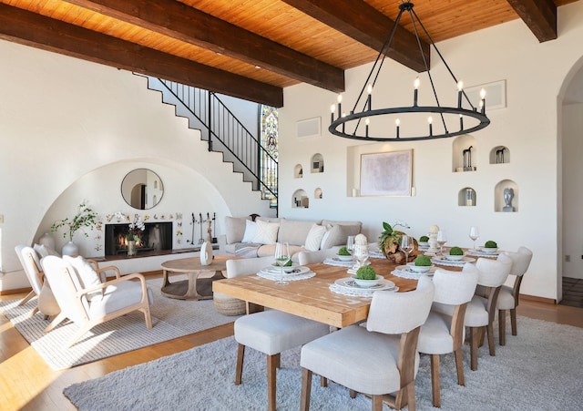 dining area with wood finished floors, arched walkways, a warm lit fireplace, wood ceiling, and a notable chandelier