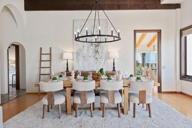 dining room featuring wood finished floors, baseboards, arched walkways, beamed ceiling, and a notable chandelier