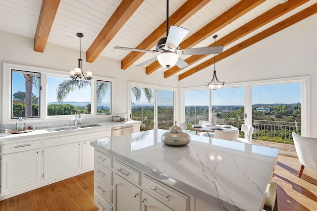 kitchen with light stone countertops, white cabinetry, lofted ceiling with beams, a sink, and stainless steel dishwasher