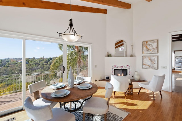 dining area featuring beamed ceiling, a fireplace, a towering ceiling, and wood finished floors