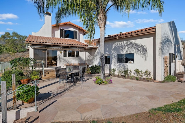 rear view of house featuring stucco siding, a patio, a chimney, and a tile roof