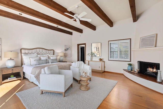 bedroom with beamed ceiling, a lit fireplace, and wood finished floors