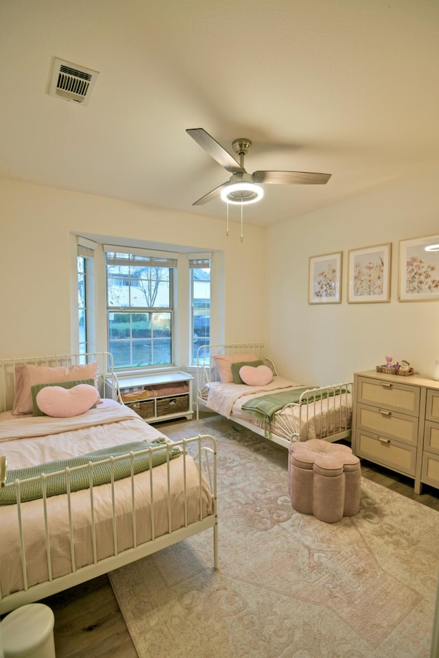 bedroom with wood finished floors, visible vents, and ceiling fan