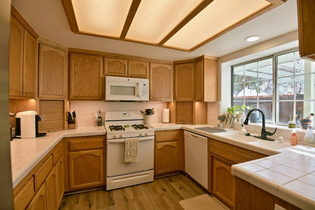 kitchen with tasteful backsplash, tile countertops, light wood-style flooring, white appliances, and a sink