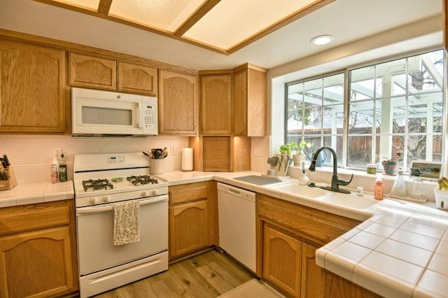 kitchen with a sink, tile countertops, white appliances, light wood finished floors, and decorative backsplash