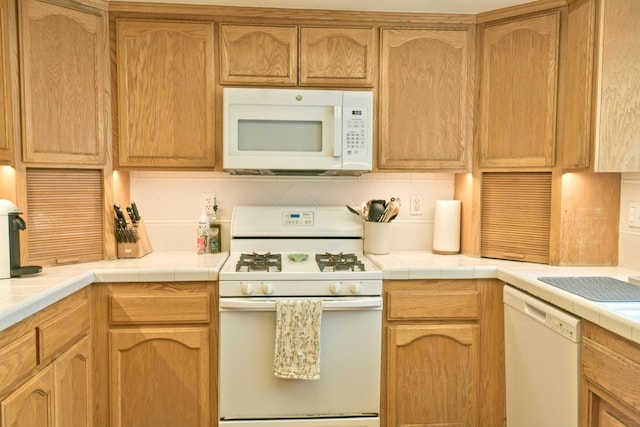 kitchen featuring tile countertops, decorative backsplash, and white appliances