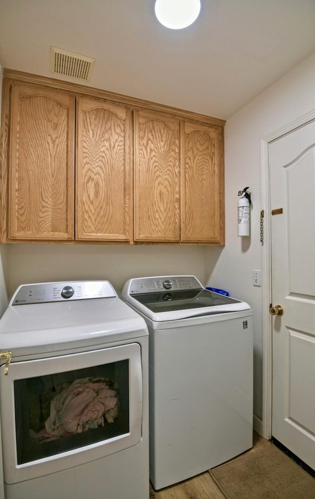 laundry room with washer and clothes dryer, visible vents, cabinet space, and light wood-type flooring